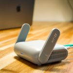 Roteador Wi‑Fi branco com antenas e cabo sobre uma mesa de madeira.