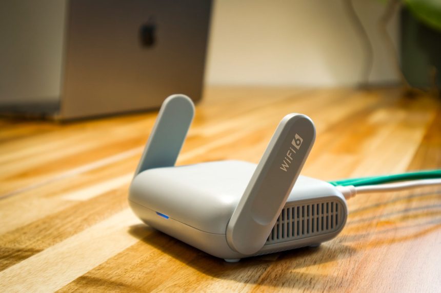 Roteador Wi‑Fi branco com antenas e cabo sobre uma mesa de madeira.