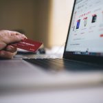 Pessoa usando cartão de crédito para fazer uma compra online em um laptop.