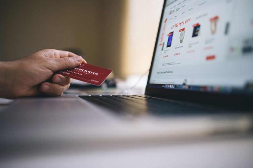 Pessoa usando cartão de crédito para fazer uma compra online em um laptop.