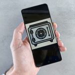 Mão segura um smartphone que exibe um ícone de segurança na tela.