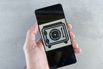Mão segura um smartphone que exibe um ícone de segurança na tela.