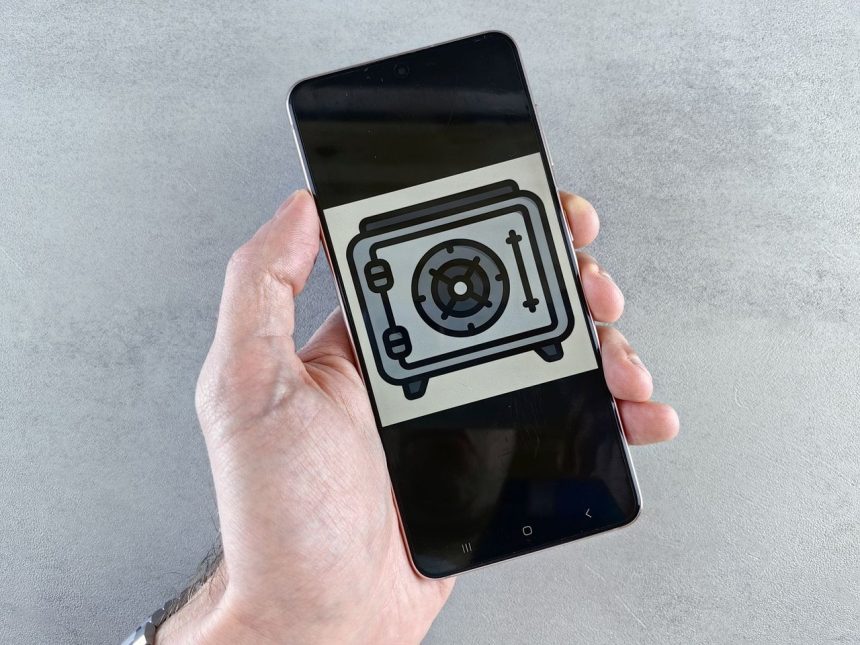 Mão segura um smartphone que exibe um ícone de segurança na tela.