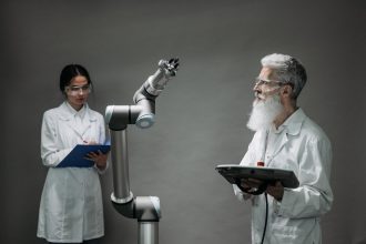 Dois cientistas trabalham com um braço robótico em um laboratório.