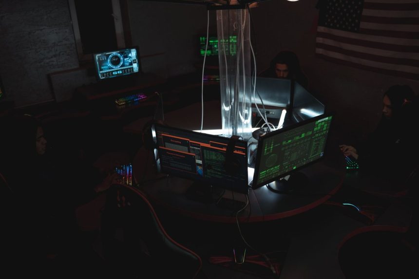 Equipe de profissionais trabalha diante de computadores em uma sala escura, em atividade relacionada à segurança cibernética