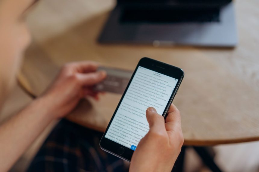 Pessoa segura um smartphone e um cartão de crédito, representando uma compra online pelo celular.